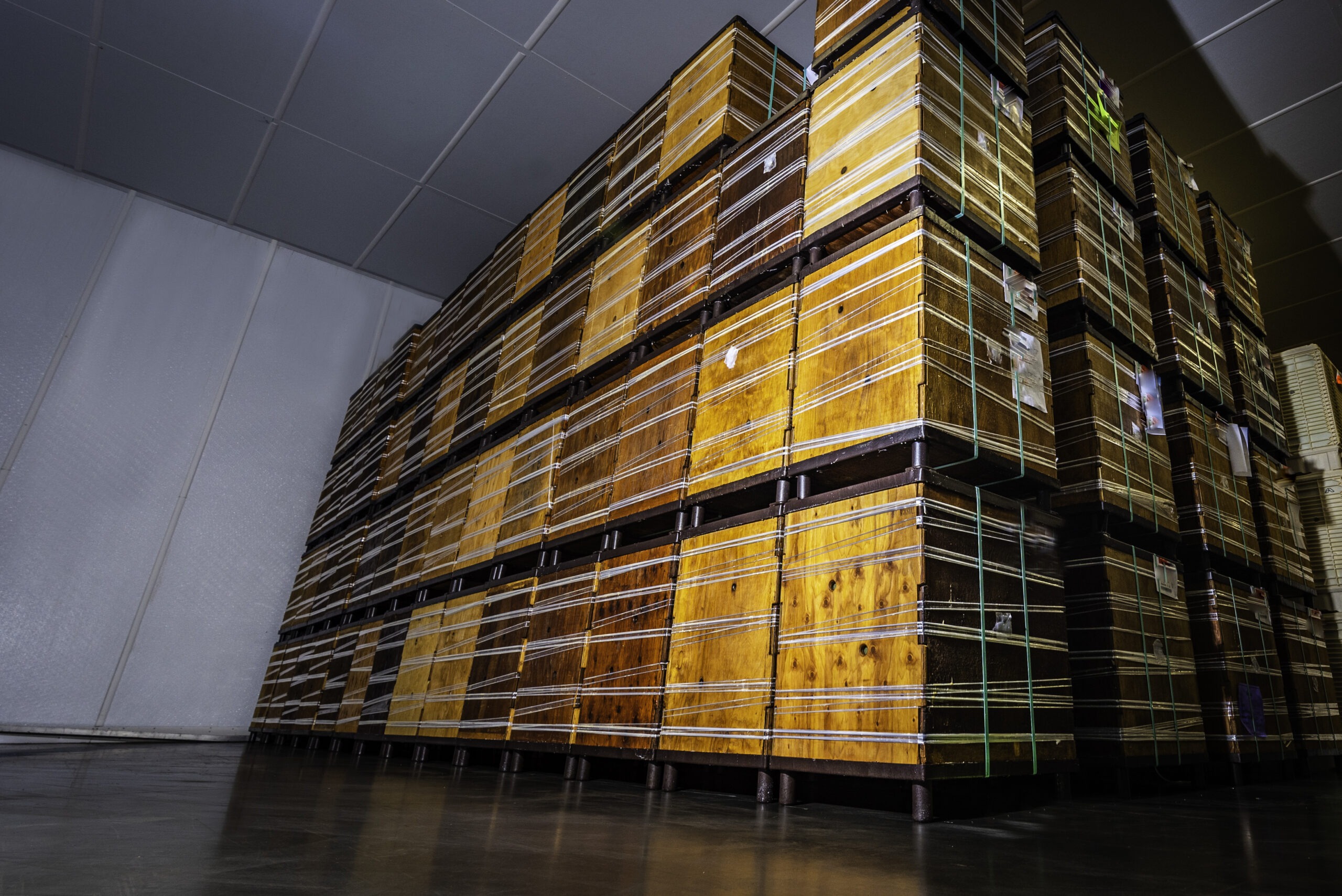 Wooden pallets stacked high and secured with green straps in warehouse