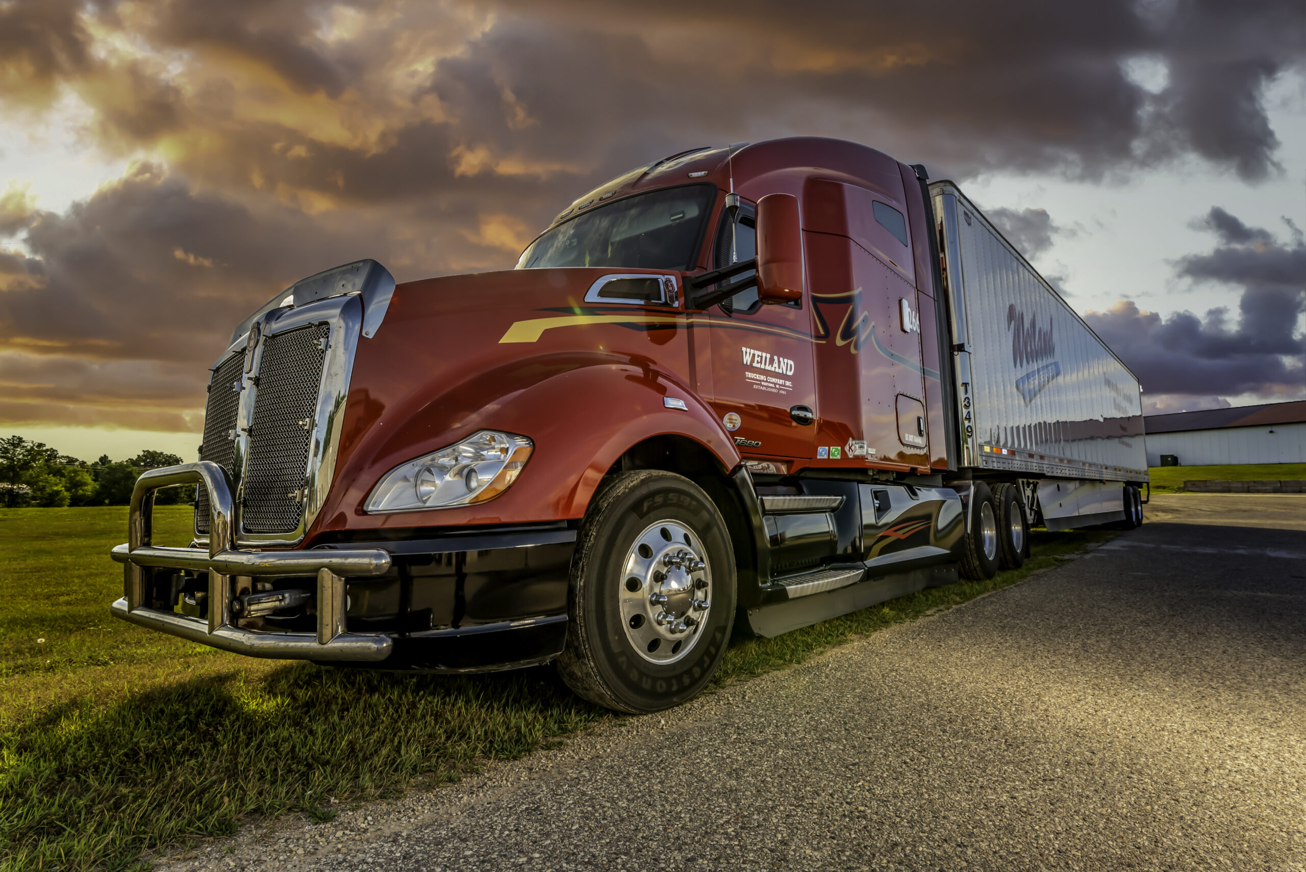 Red Weiland semi-truck with refrigerated trailer parked on roadside at sunset