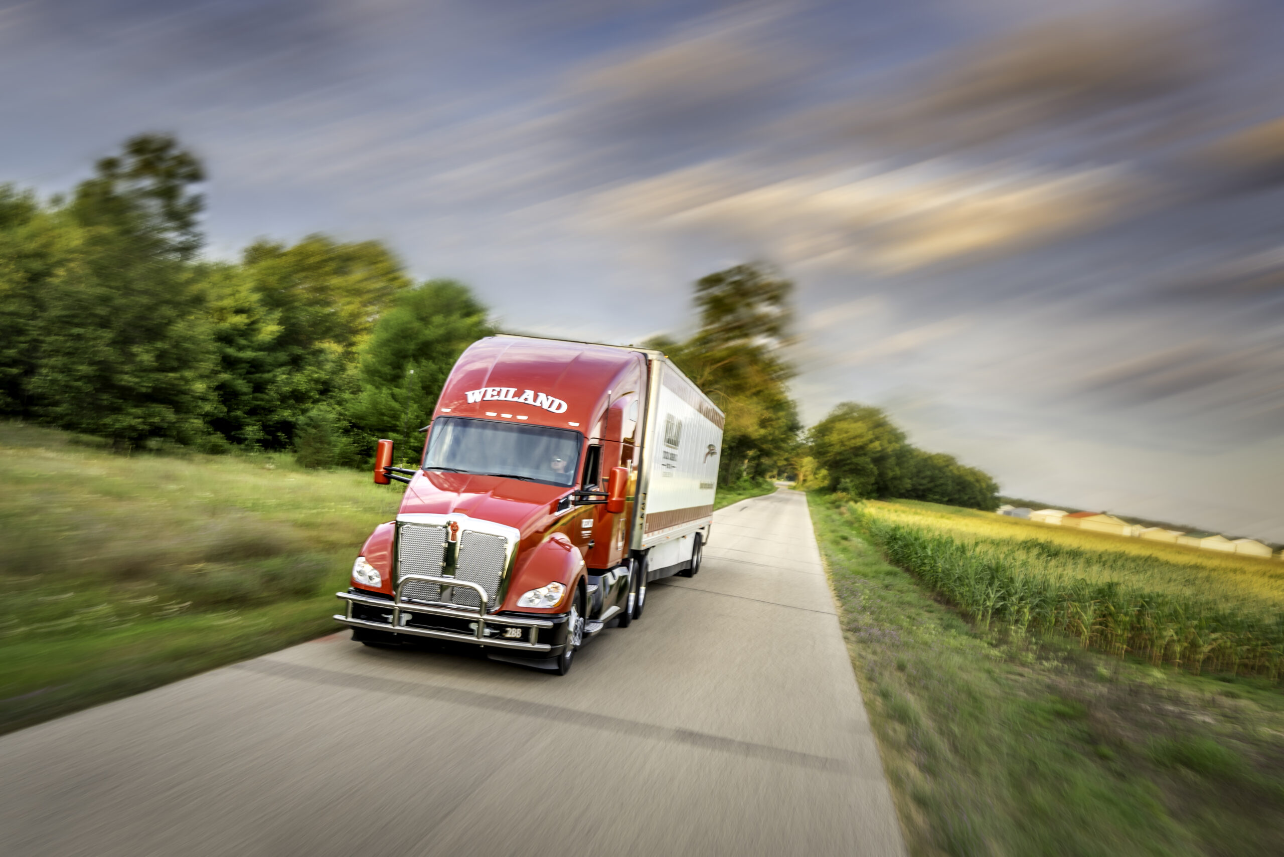 Red Weiland semi-truck with refrigerated trailer driving on rural highway with motion blur