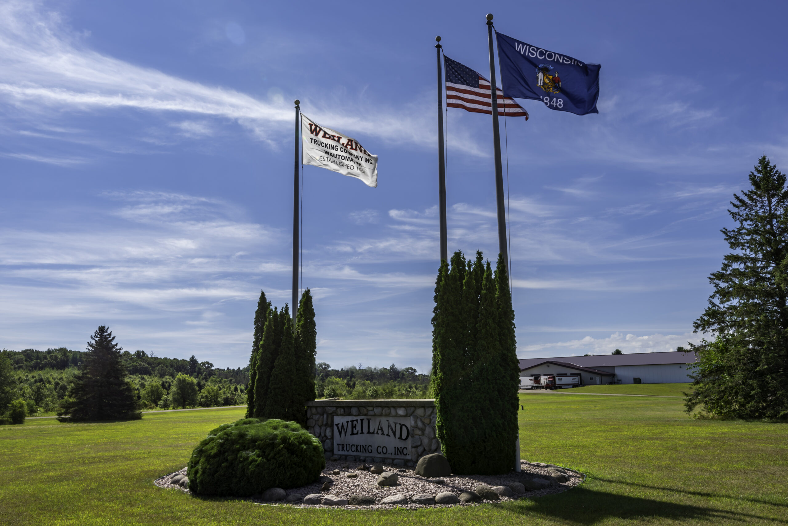Weiland Trucking stone sign with American and Wisconsin flags on landscaped grounds